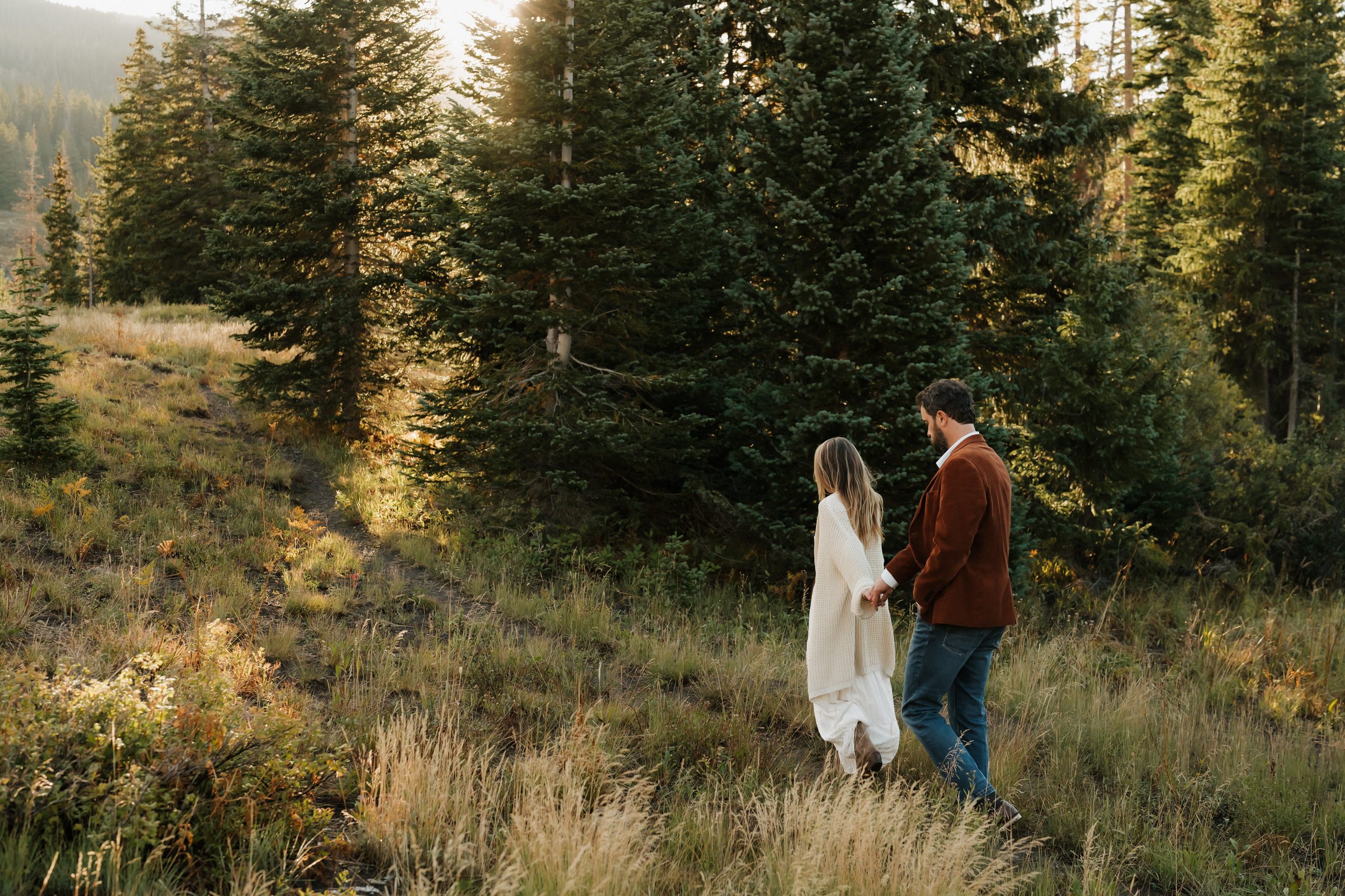 Colorado Engagement Session Locations Couple walking through a sunlit pine forest during Cooper and Paige's sunrise Colorado engagement session