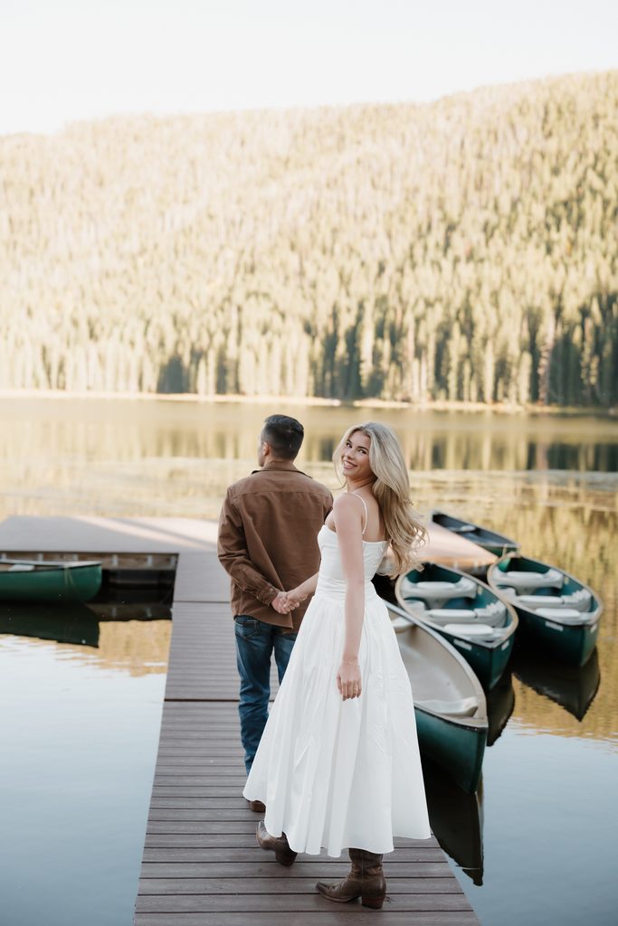 Colorado Engagement Session Locations Engaged couple standing beside Piney Lake near Vail with mountain reflections during their Colorado engagement session