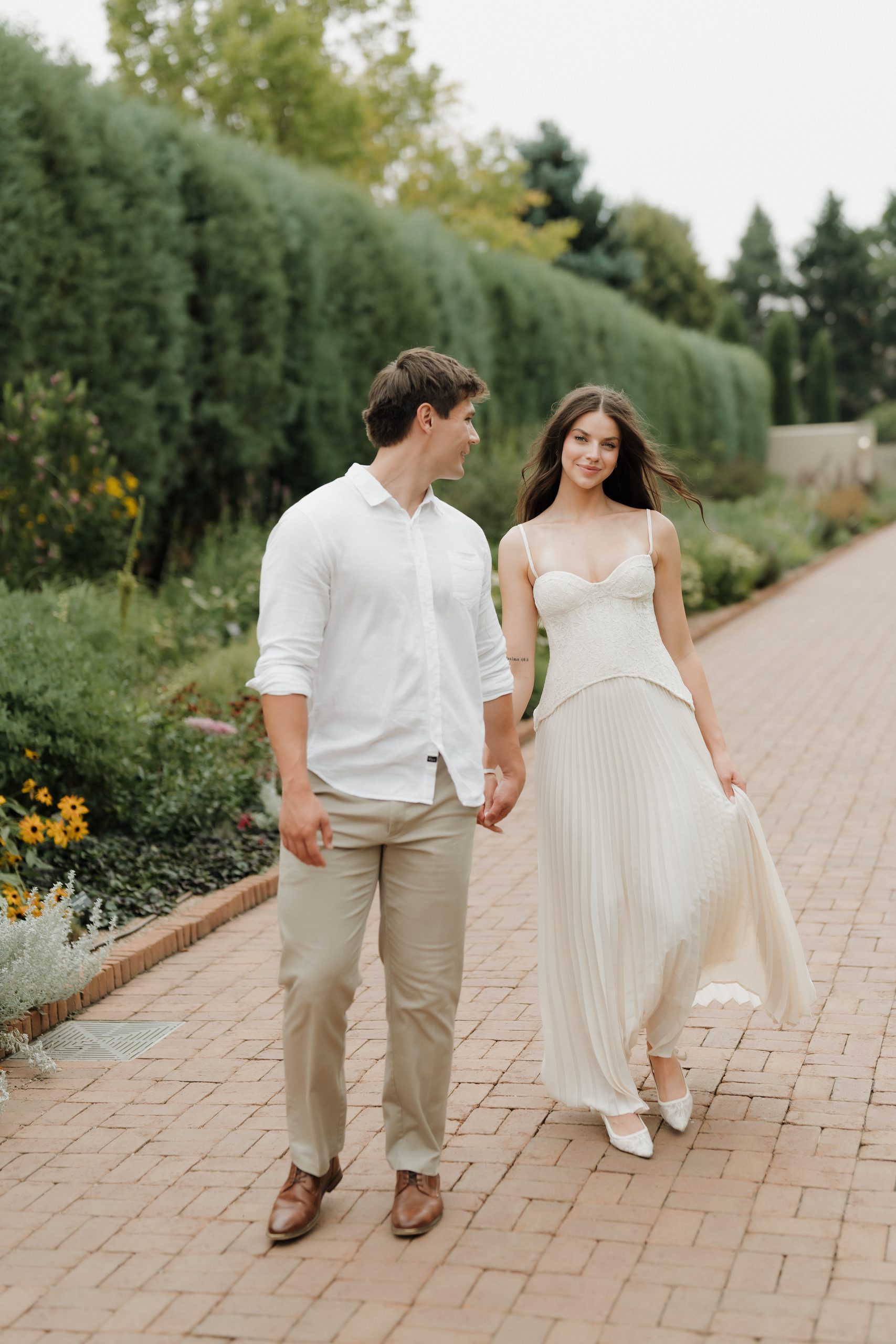 Colorado Engagement Session Locations Couple walking hand in hand along a garden path during their Denver Botanic Gardens Colorado engagement session