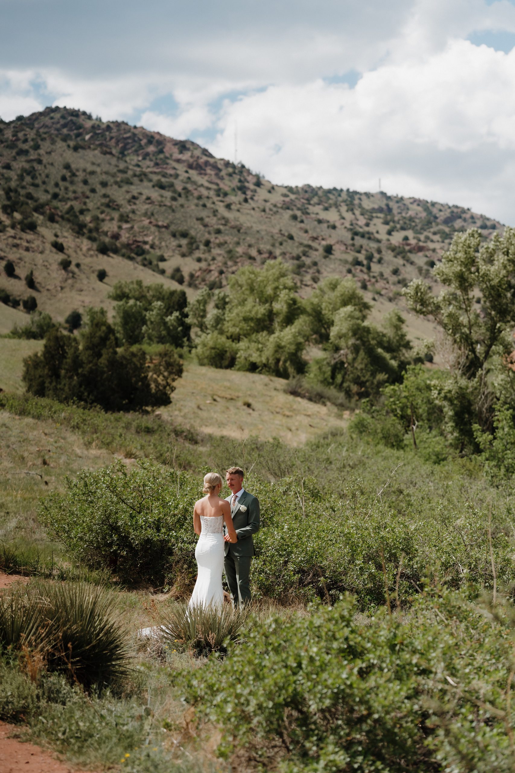 Colorado Engagement Session Locations Couple walking hand in hand through a green field during their Red Rocks Colorado engagement session