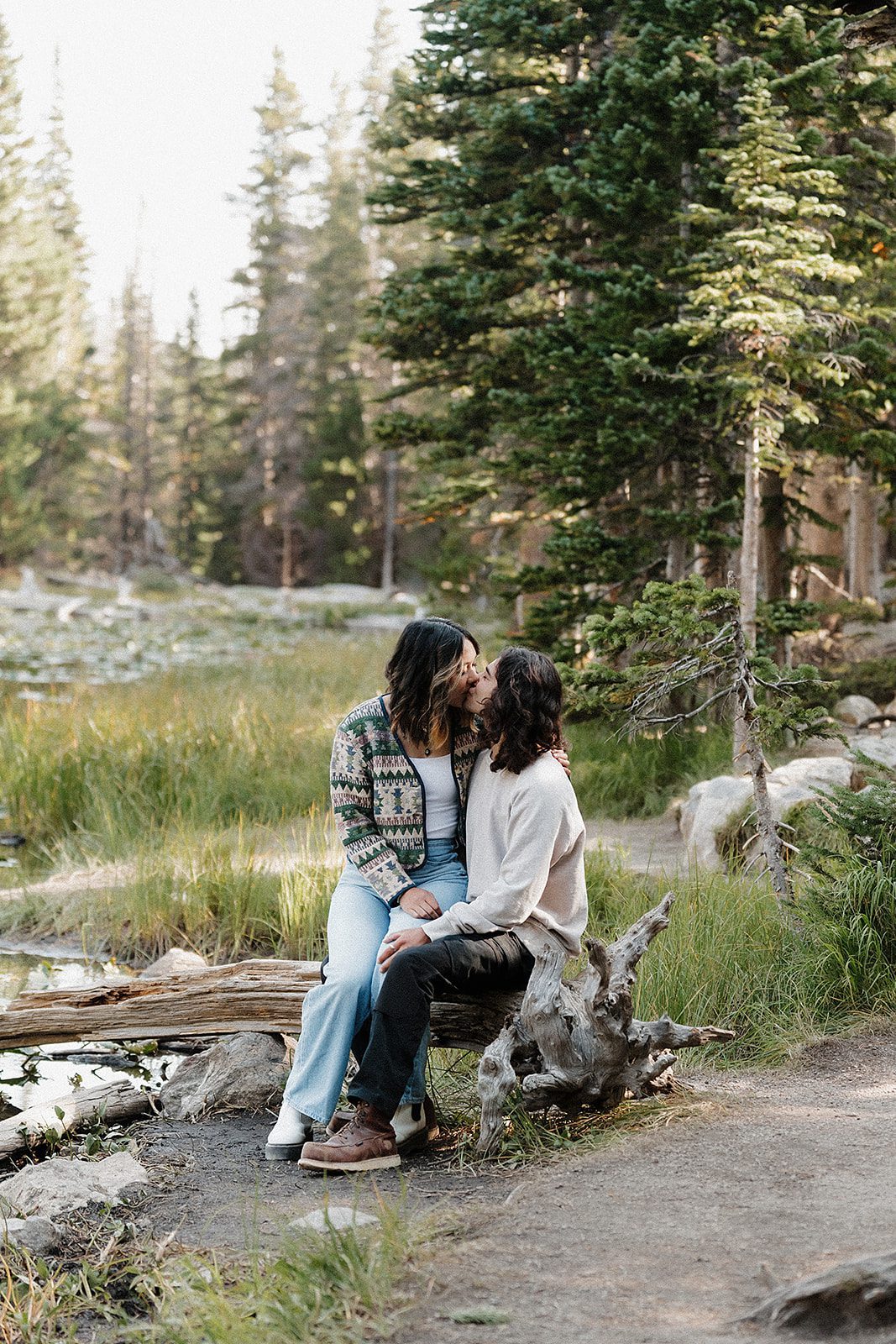 Couple kissing while seated on a driftwood log beside an alpine stream in Colorado