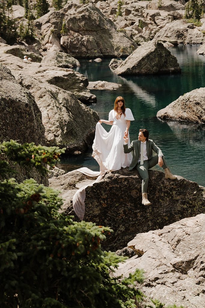 Elopement couple posing on rocky ledge above a vivid turquoise alpine lake in Colorado