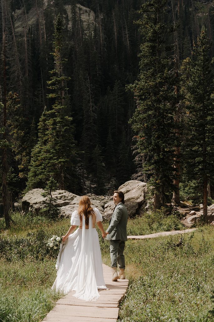 Rocky Mountain National Park elopement couple walking hand in hand down a wooden boardwalk trail through alpine forest