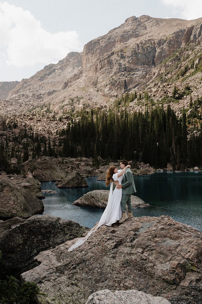 Rocky Mountain National Park elopement couple at Dream Lake shoreline with veil trailing across the rocks