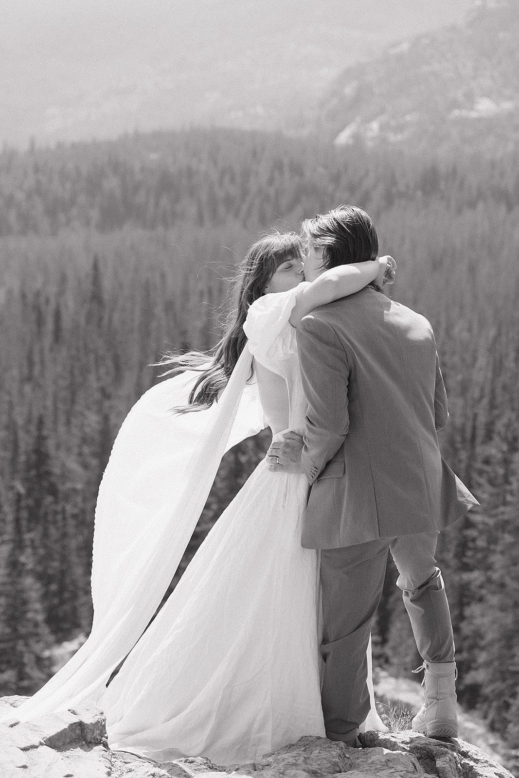 Rocky Mountain National Park elopement first kiss in black and white with forested Colorado mountains in the background