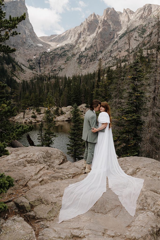 Newlyweds embracing on rocky overlook above a turquoise alpine lake in Colorado after their elopement