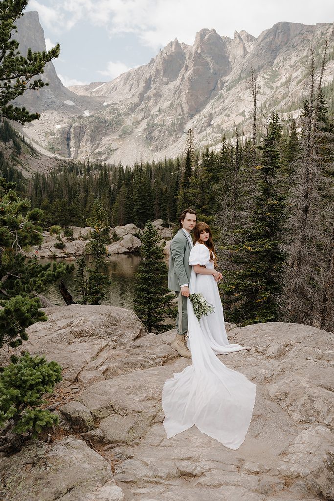 Newlyweds embracing on rocky overlook above a turquoise alpine lake in Colorado after their elopement
