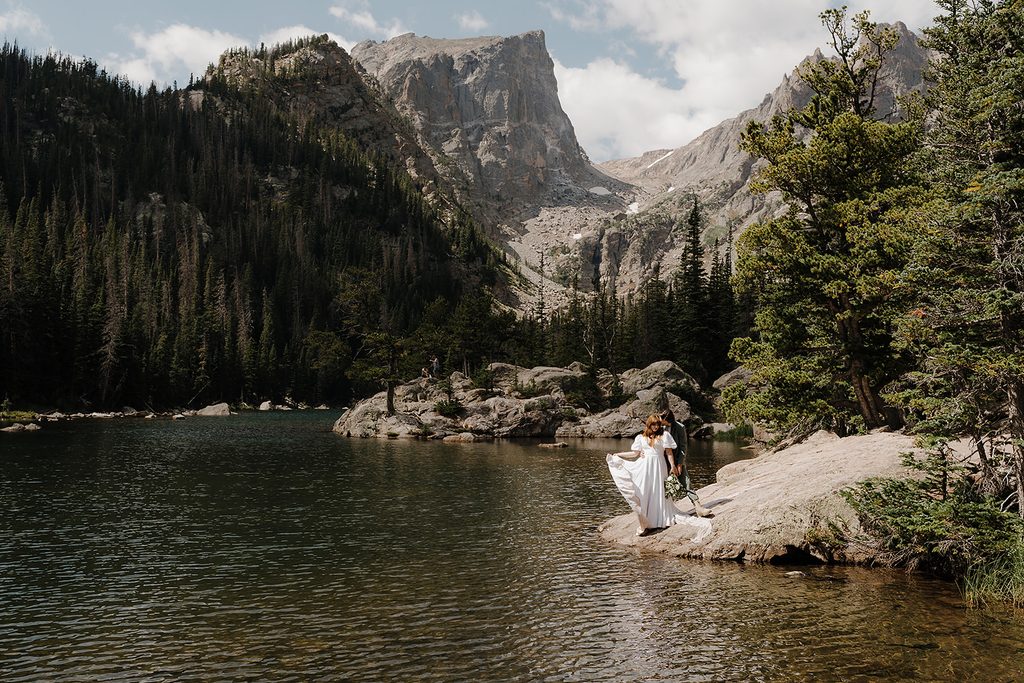 Newlyweds embracing on rocky overlook above a turquoise alpine lake in Colorado after their elopement