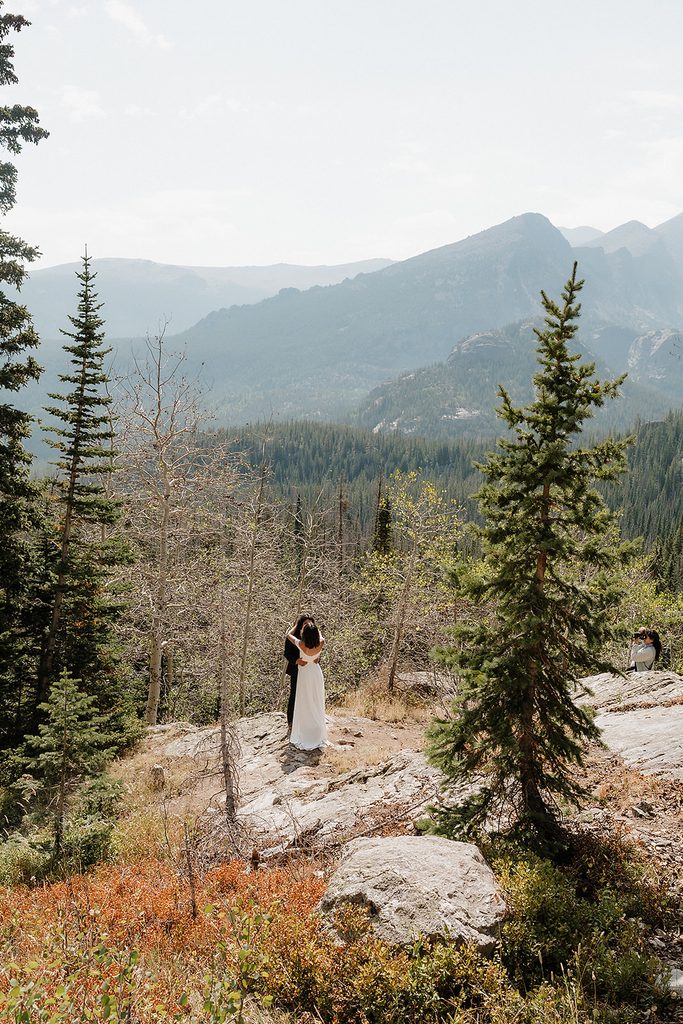 Rocky Mountain National Park elopement couple embracing on boulder surrounded by pine trees and mountain peaks