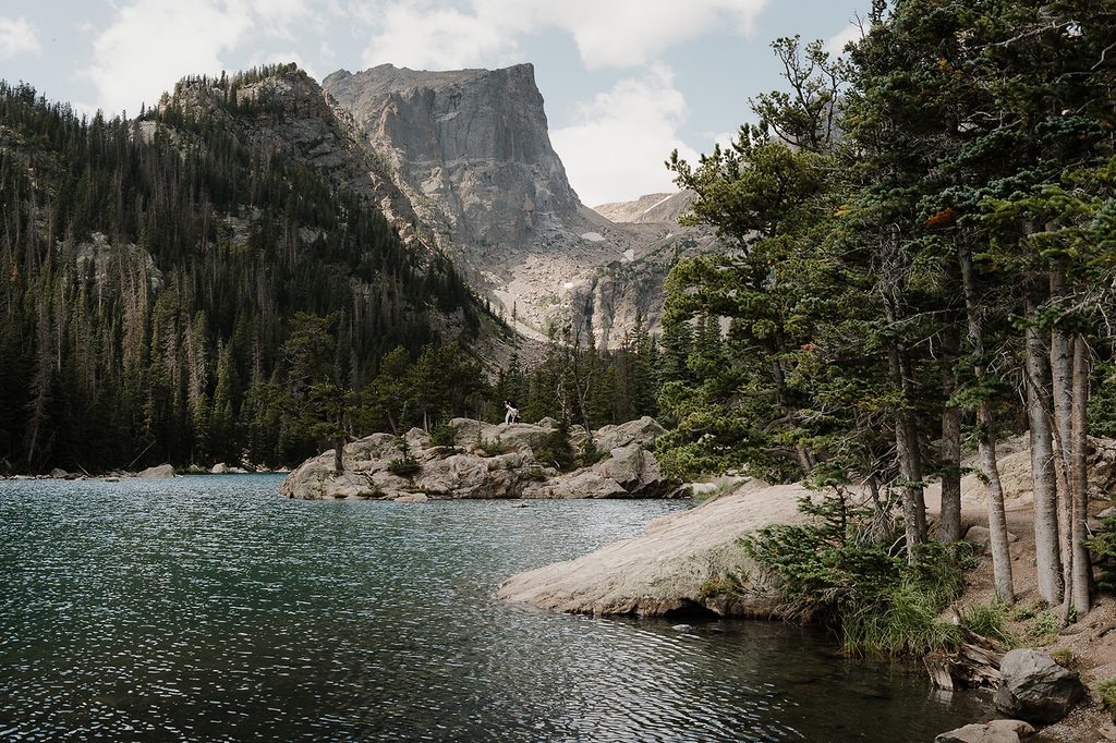 Wide landscape view of Dream Lake Colorado with couple in elopement attire visible on rocks at the water's edge