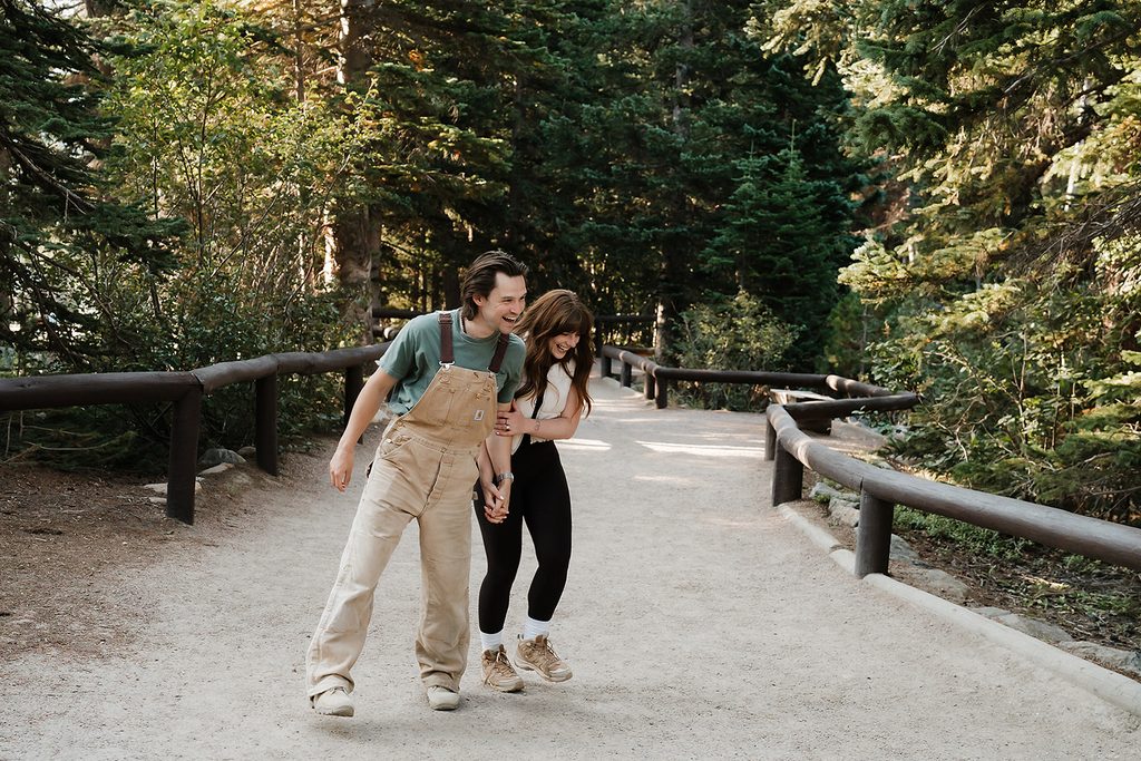 Couple laughing and walking together along a trail through Rocky Mountain National Park during their Colorado engagement photos
