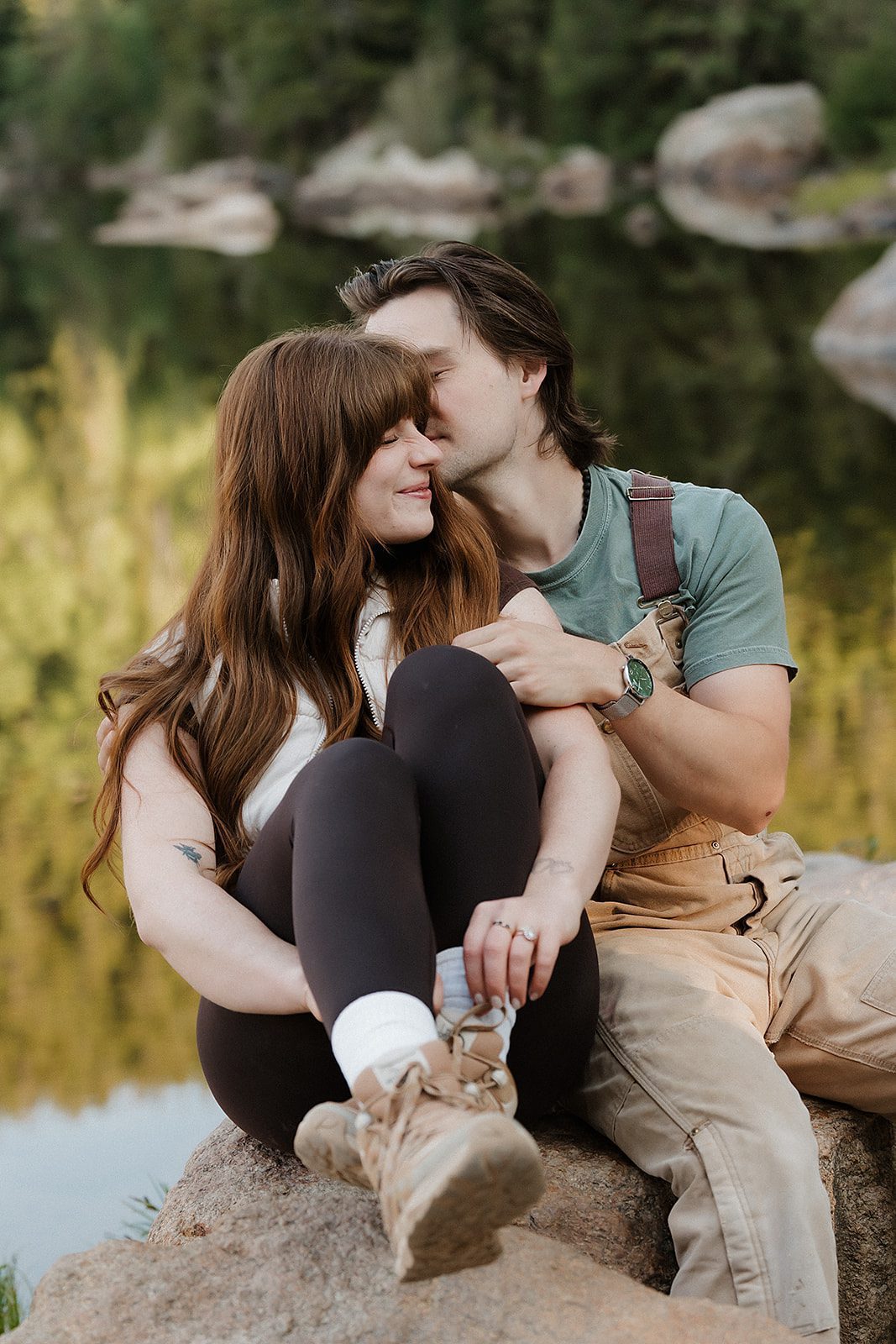 Engaged couple sitting close on a lakeside boulder sharing a quiet moment during their Rocky Mountain National Park engagement session