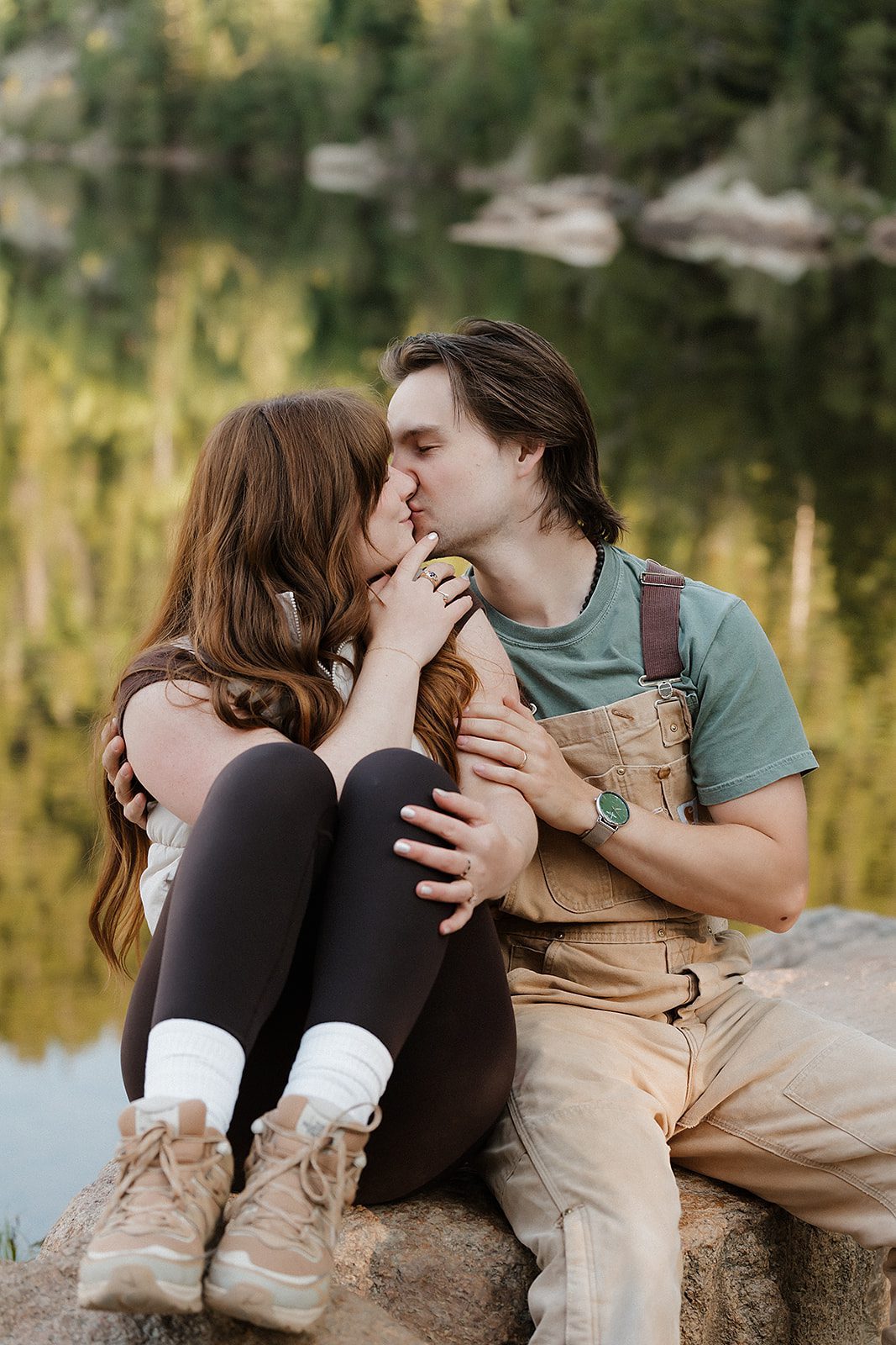 Engaged couple sitting close on a lakeside boulder sharing a quiet moment during their Rocky Mountain National Park engagement session