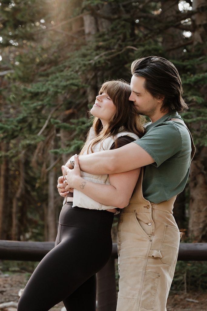 Couple posing together against a wooden trail railing in golden afternoon light during Colorado engagement photos at RMNP